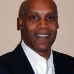 Portrait of a smiling man in a dark suit and white shirt.