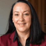 Portrait of a smiling woman with long dark hair and a maroon blazer.