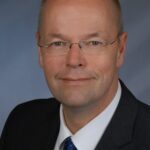 Professional portrait of a middle-aged man wearing glasses and a suit.