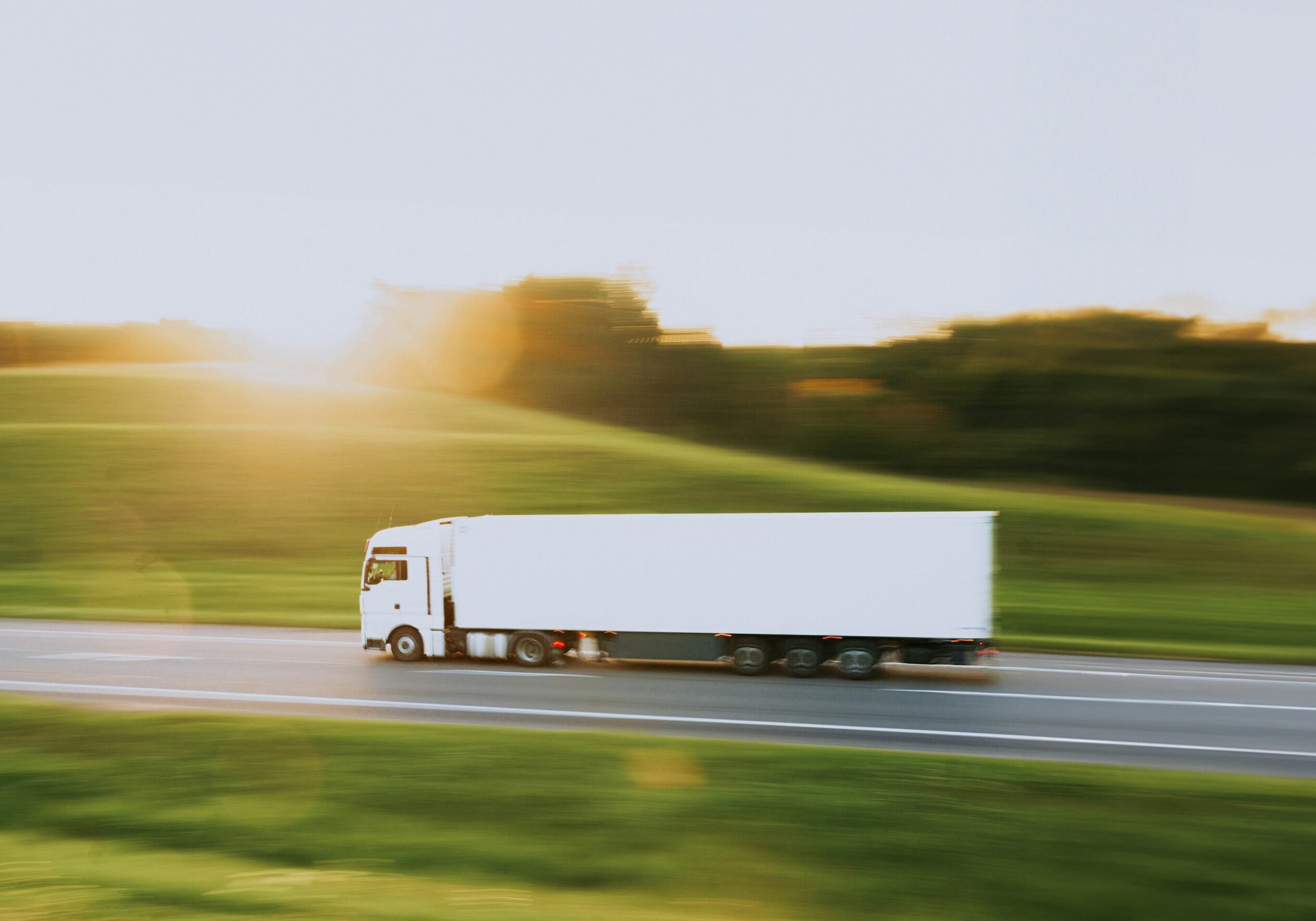 A white semi-truck driving on a highway during sunset.
